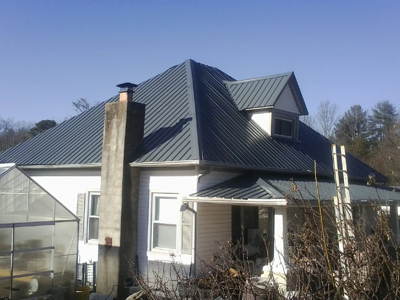 Dark blue standing seam metal roof on a white farmhouse with dormer — Slate & Tile Roof Repair by Roofing Brothers in Mountain View